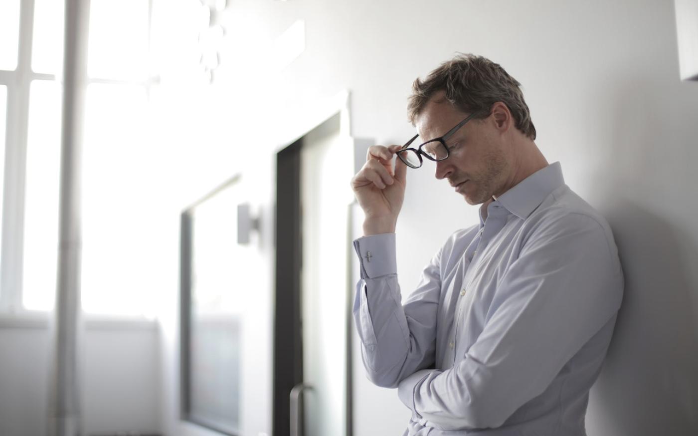 Man with glasses leaning against a wall