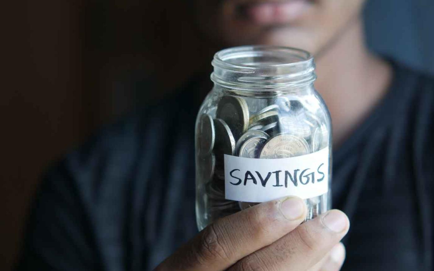 Person holding jar of coins with a 'savings' label